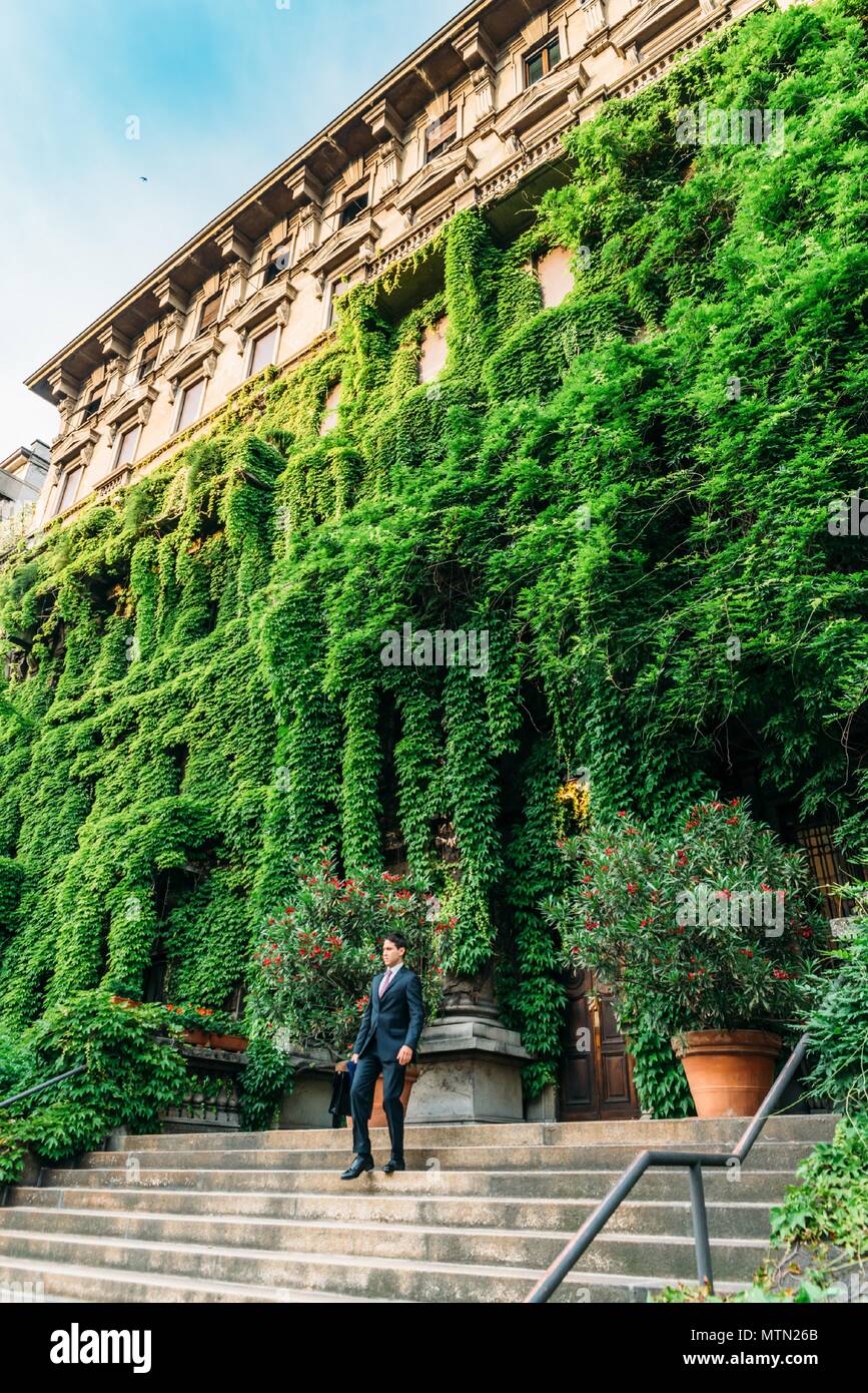 A Milanese man dressed in a suit walk down steps from a palace in Viale Luigi Majno covered in leaves, Lombardy, Italy Stock Photo