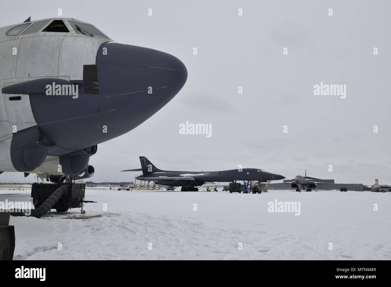 The nose of a B-52H Stratofortress in natural metal with gunship grey components frames a B-1B Lancer in the background on a snowy flight line at the Oklahoma City Air Logistics Complex Jan. 6, 2017, Tinker Air Force Base, Oklahoma. Despite the rare accumulation of snow, the important maintenance and sustainment operations conducted by the OC-ALC continue to ensure aircraft production stays on track to deliver capability to the warfighter. (U.S. Air Force photo/Greg L. Davis) Stock Photo