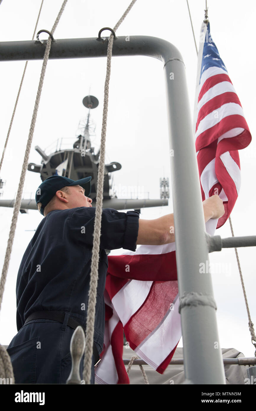 170112-N-XT039-130 SASEBO, Japan (Jan. 12, 2017) Quartermaster 1st Class Matthew Lenerville, from Richardton, N.D., ceremoniously lowers an American flag on the main masthead of amphibious assault ship USS Bonhomme Richard (LHD 6) in honor of a U.S. Navy Captain’s retirement. Lenerville raised the flag to honor a U.S. Navy Captain’s retirement. The ceremony is performed at the request of the retiree. The retiree mails the flag to the ship and a flag certificate, signed by the ship’s commanding officer, is sent to the retiree when the flag is returned. Bonhomme Richard, forward-deployed to Sase Stock Photo