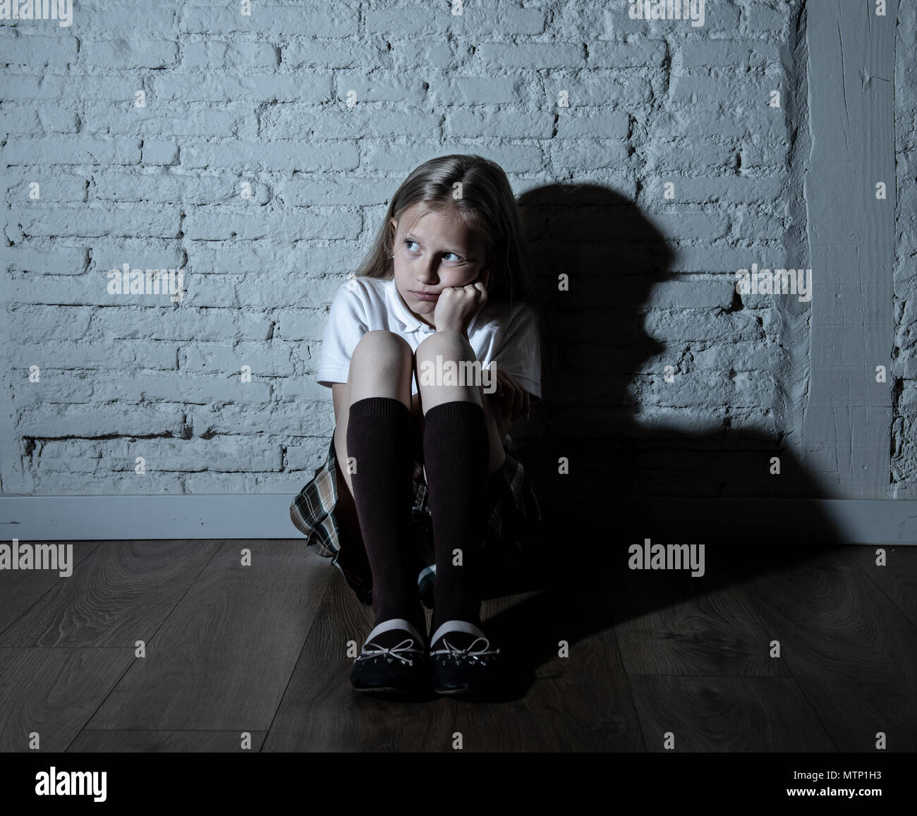 Sad desperate young girl suffering from bulling and harassment felling lonely, unhappy desperate and hopeless sitting against the wall, dark light. Sc Stock Photo