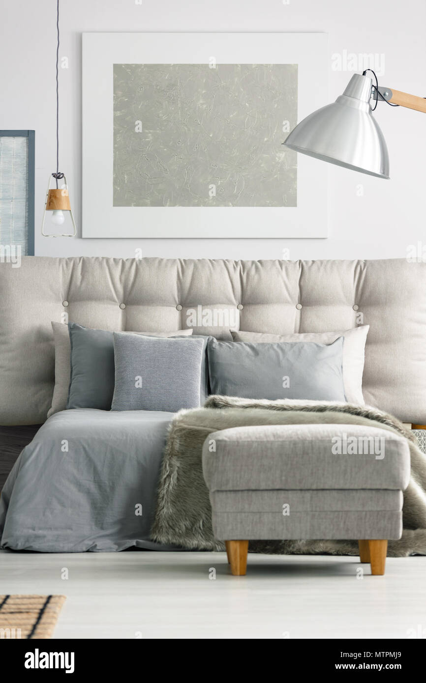 Ottoman by the grey comfortable bed in modern white bedroom Stock Photo