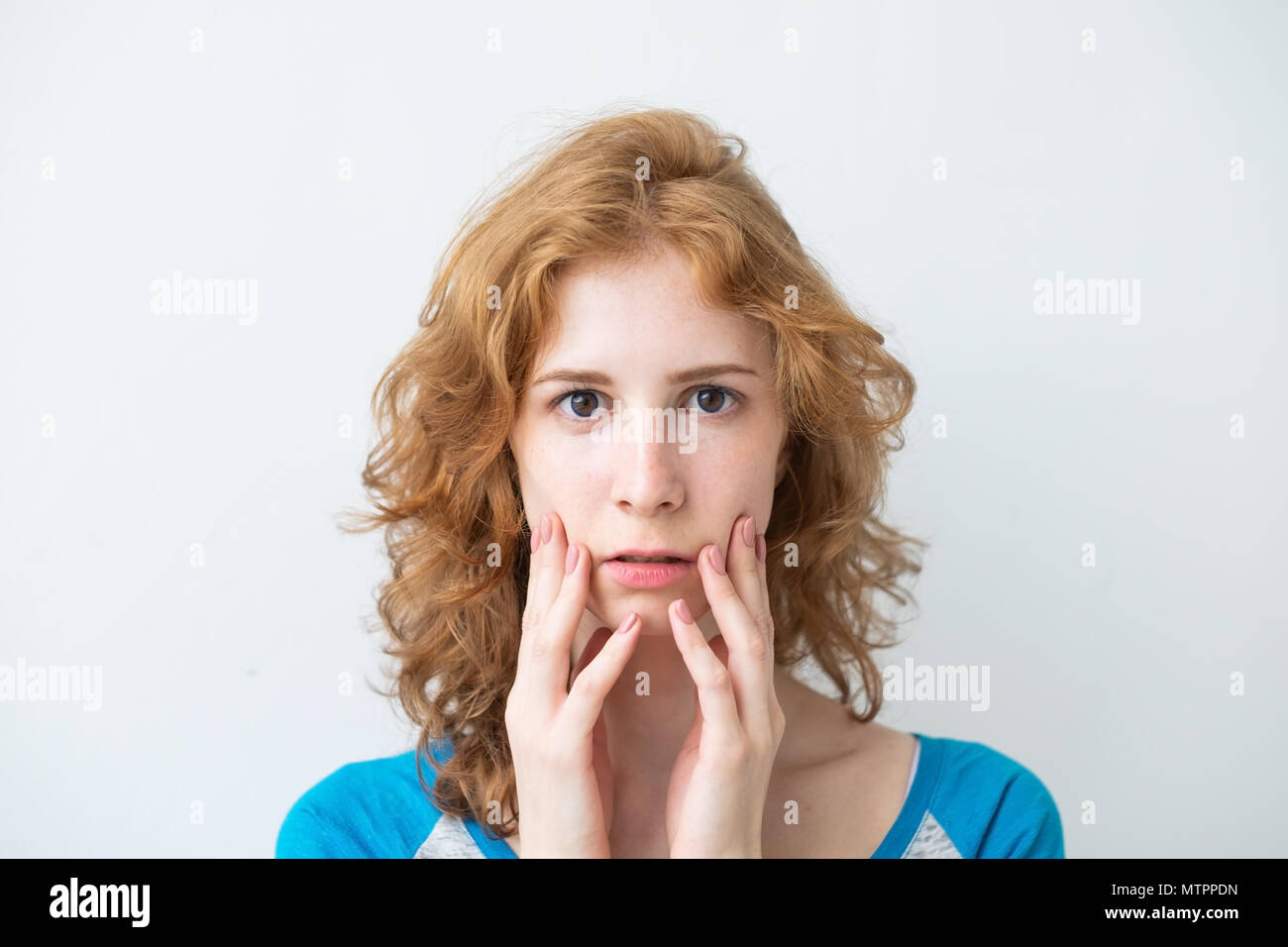 Amazed female model with red curly hair, wearing t-shirt, looking with bugged eyes Stock Photo