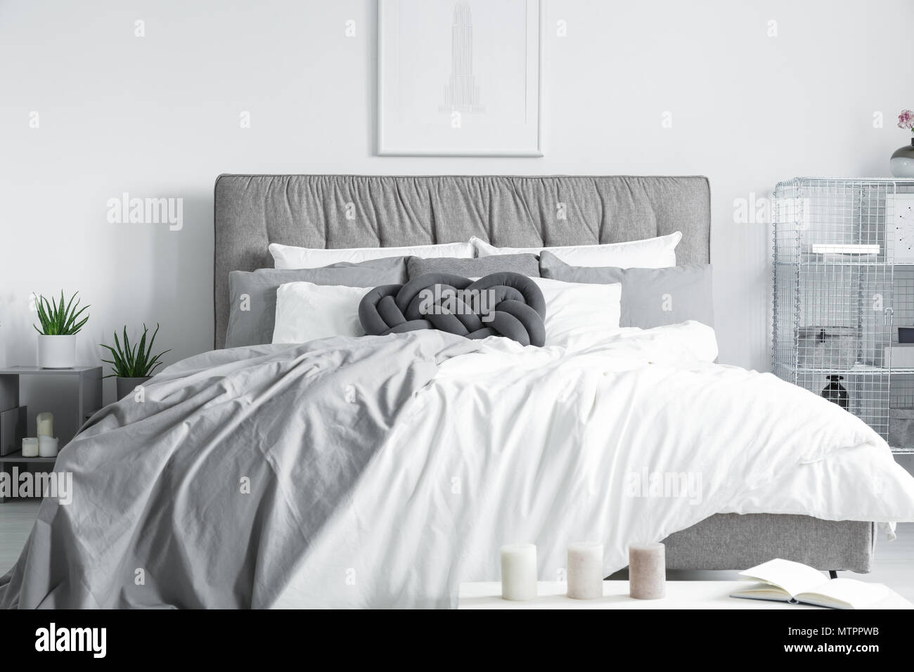 Handmade dark pillow on the big bed placed under minimalistic poster