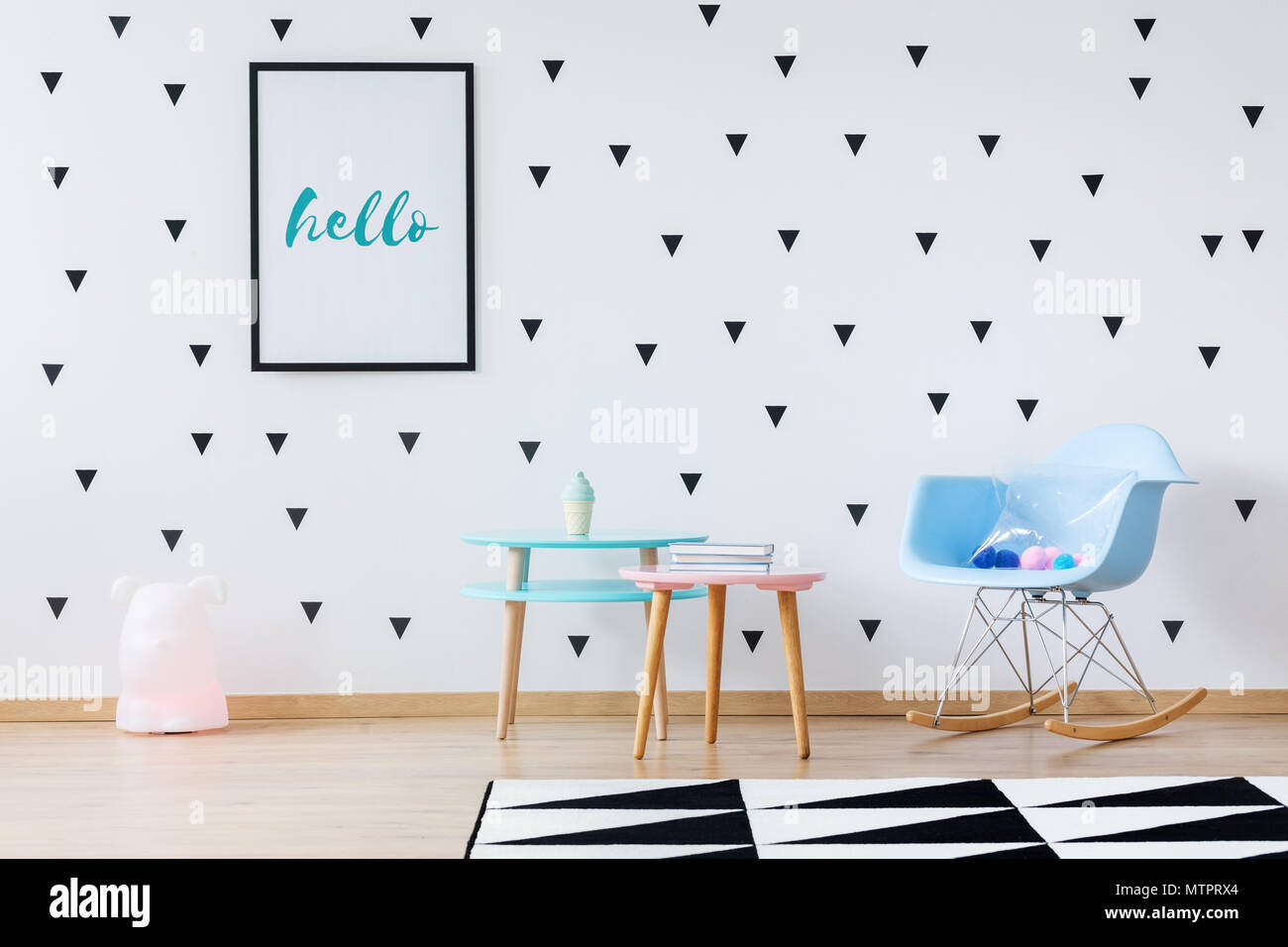 Toys on blue rocking chair next to wooden tables against wallpaper with black triangles in a play room with geometric carpet Stock Photo