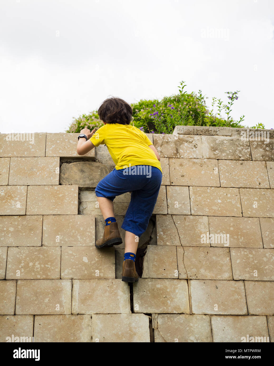 Young boy of ten climbs on a wall. Humpty Dumpty sat on a wall, Humpty Dumpty had a great fall All the king’s horses and all the king’s men Couldn’t p Stock Photo