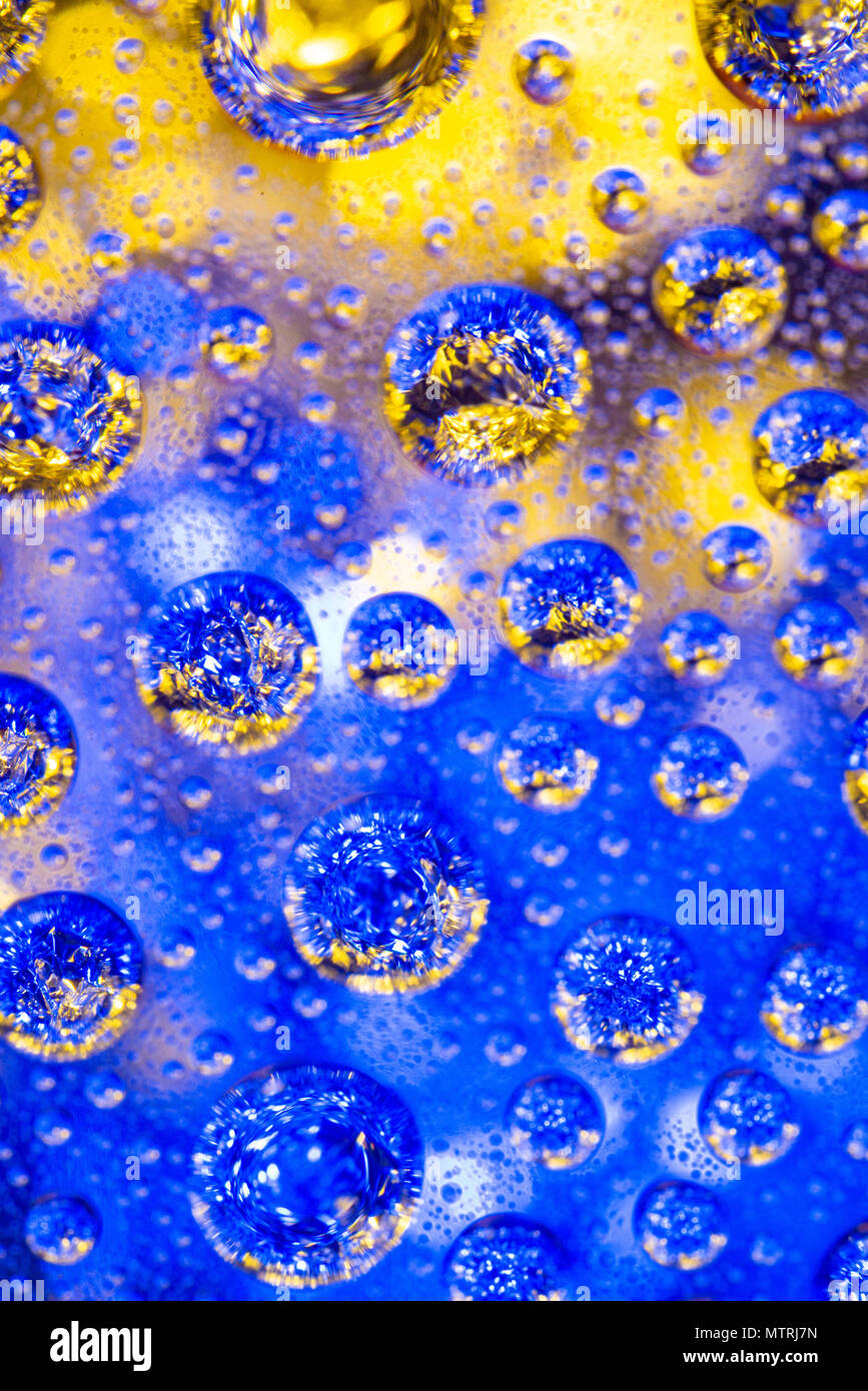 Water drops on glass with a yellow and blue lighted background. Stock Photo