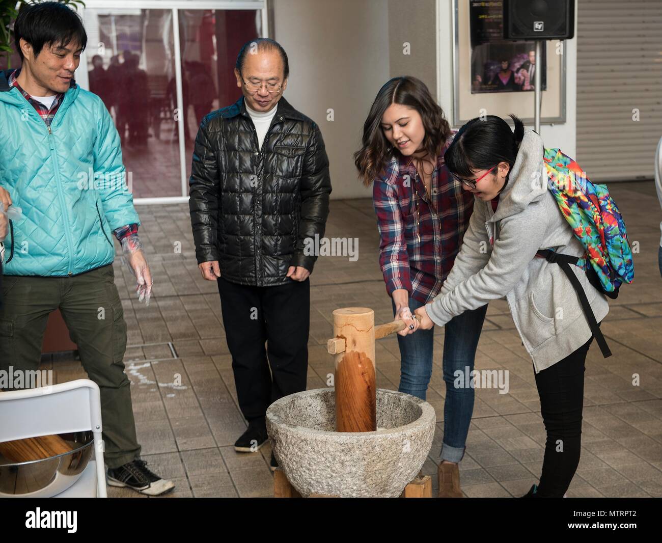 Members of the Kadena Teen Center and Okinawa City junior high school use a wooden mallet to pound rice to make mochi Jan. 21, 2017, at Koza Music City, Okinawa, Japan. The Let’s Learn English exchange builds relationships between Okinawan and American teenagers. (U.S. Air Force photo by Airman 1st Class Corey Pettis) Stock Photo