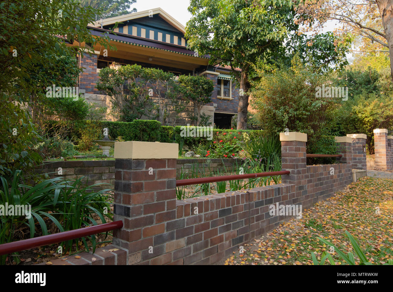 A 1928 tiled roof, double brick, gable fronted, California Bungalow home with a matching brick front fence on Sydney's north shore in NSW Australia Stock Photo