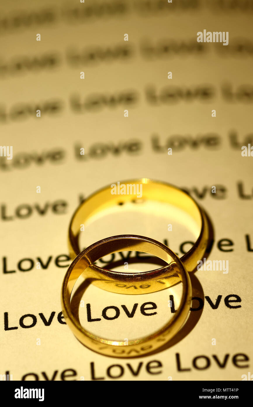 Gold wedding rings on an open book with the word love repeated on the pages Stock Photo