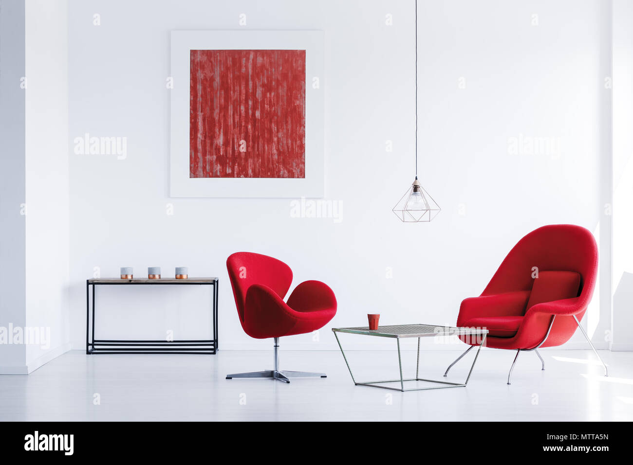 Black metal table with three candles standing in the corner of white room with red armchairs Stock Photo