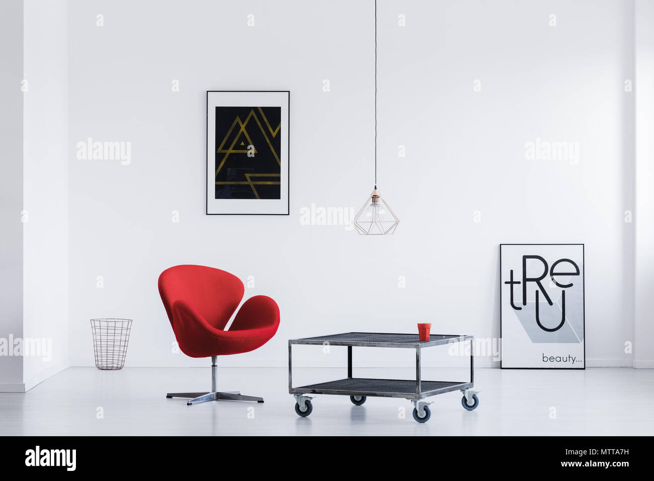 Stylish waiting room with white walls, industrial table, red armchair and modern posters Stock Photo