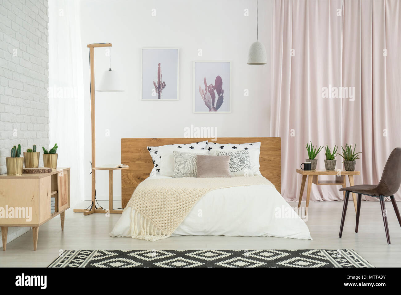 Wooden lamp standing by the bed with patterned pillows in feminine room with cacti in pots Stock Photo