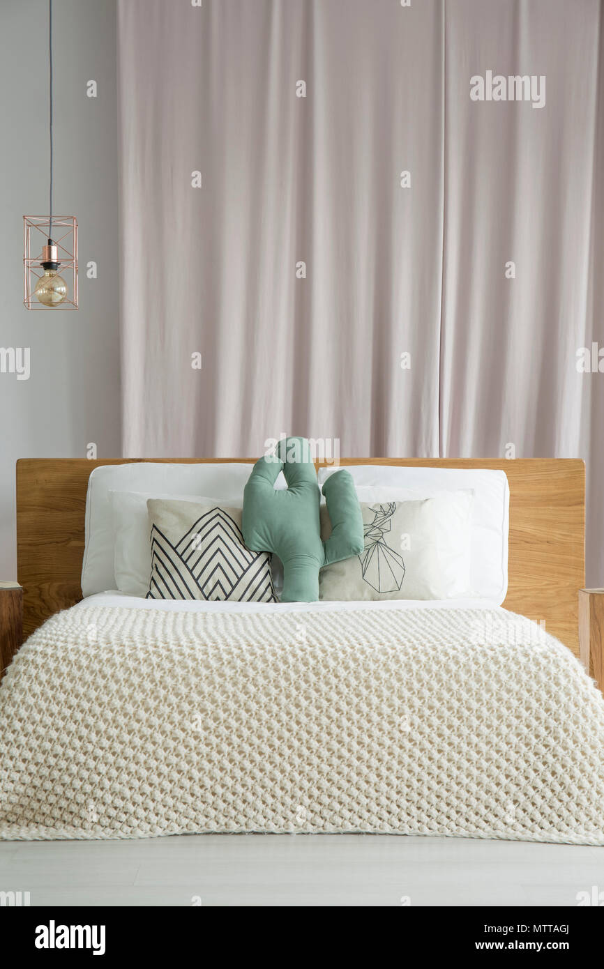 Pastel pink drape hanging behind bed with wooden bedhead and cactus