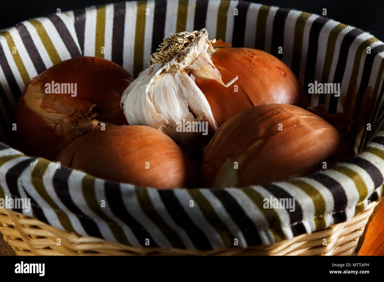 Onions and head of garlic in a wicker basket seen from up close. Rustic ...
