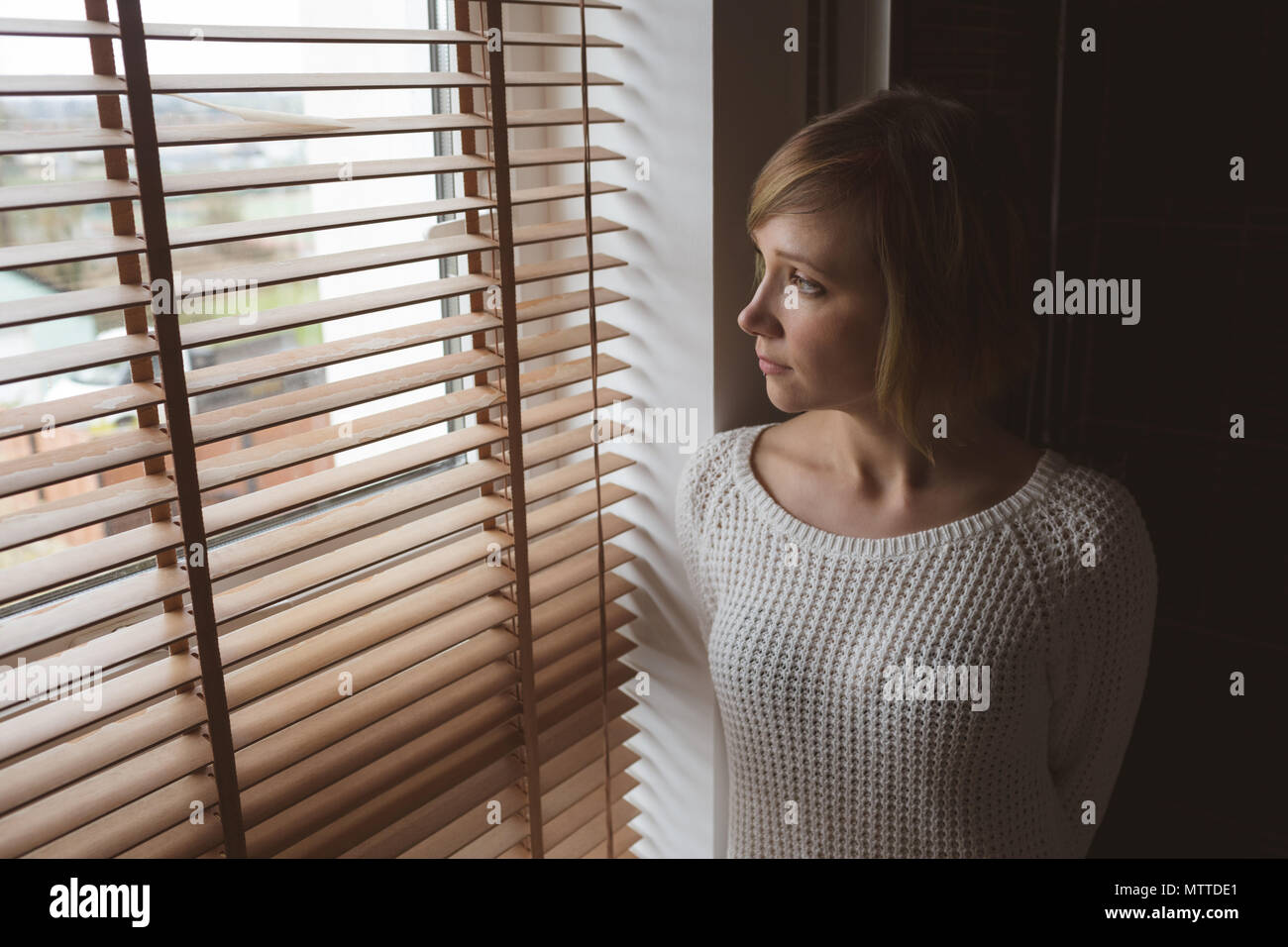 Woman looking through window blinds Stock Photo