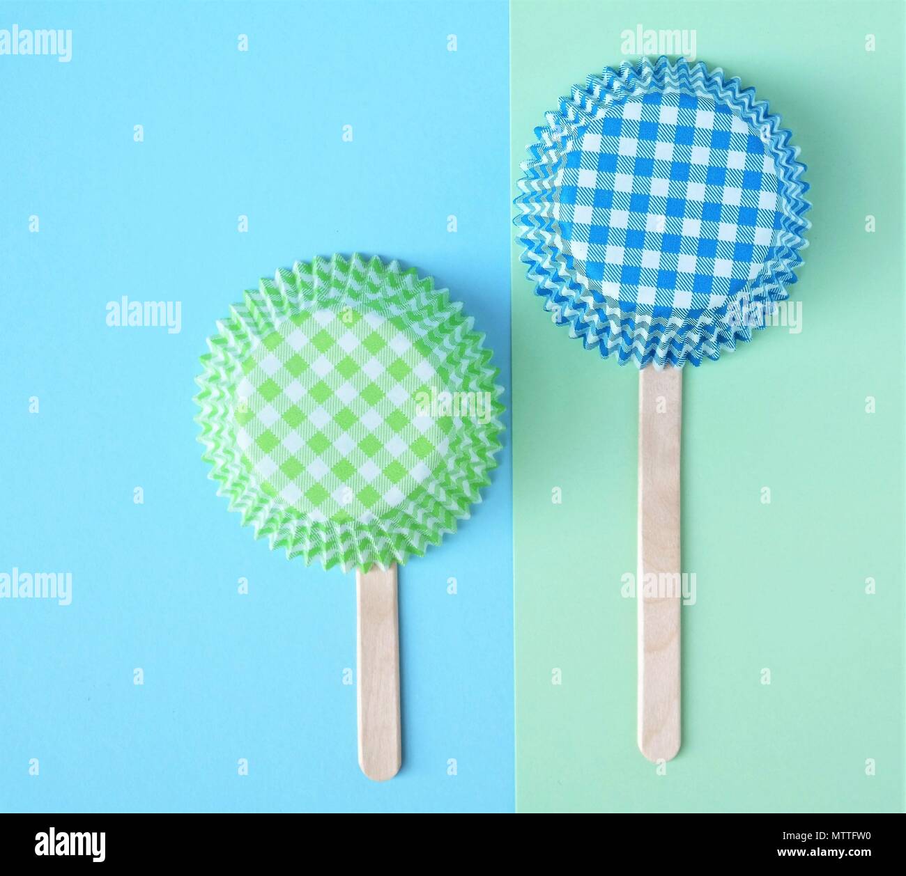 Two cupcake molds connected with a popsicle stick. Simple baking background with green and blue colors and text space. Stock Photo