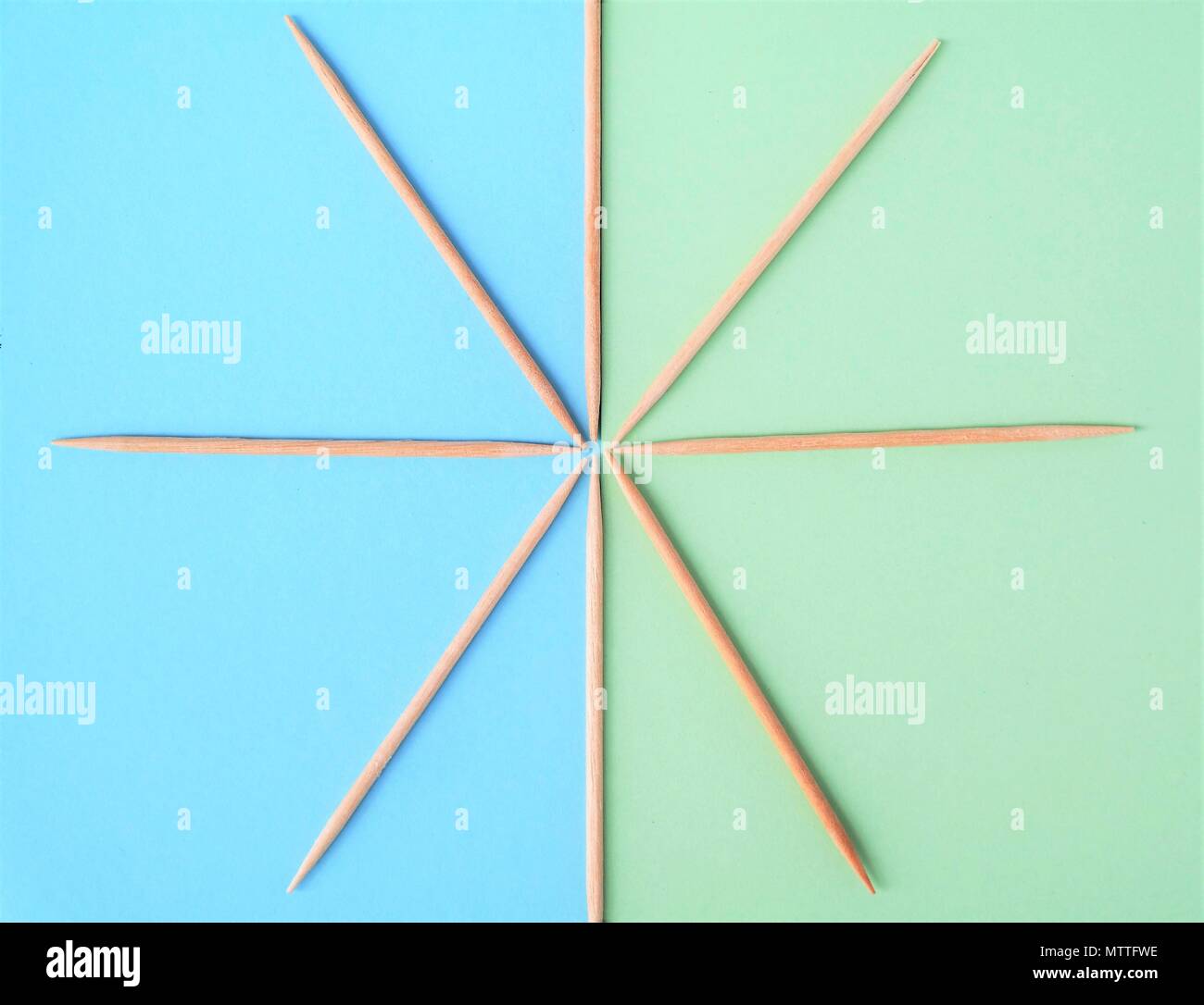 A simple picture made from eight cocktail sticks, laid down in a star shape. And two strips of paper in the background, blue and green pastel color. Stock Photo