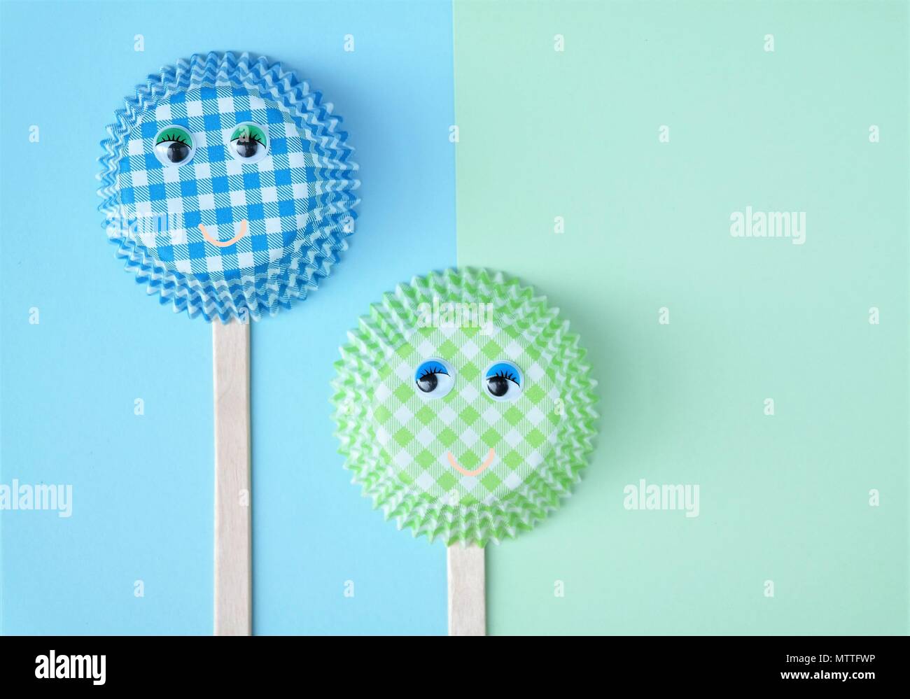 two cupcake molds with wobbly eyes, ice popsicle sticks en smiling faces. simple baking concept in green and blue colors. Funny creative image Stock Photo