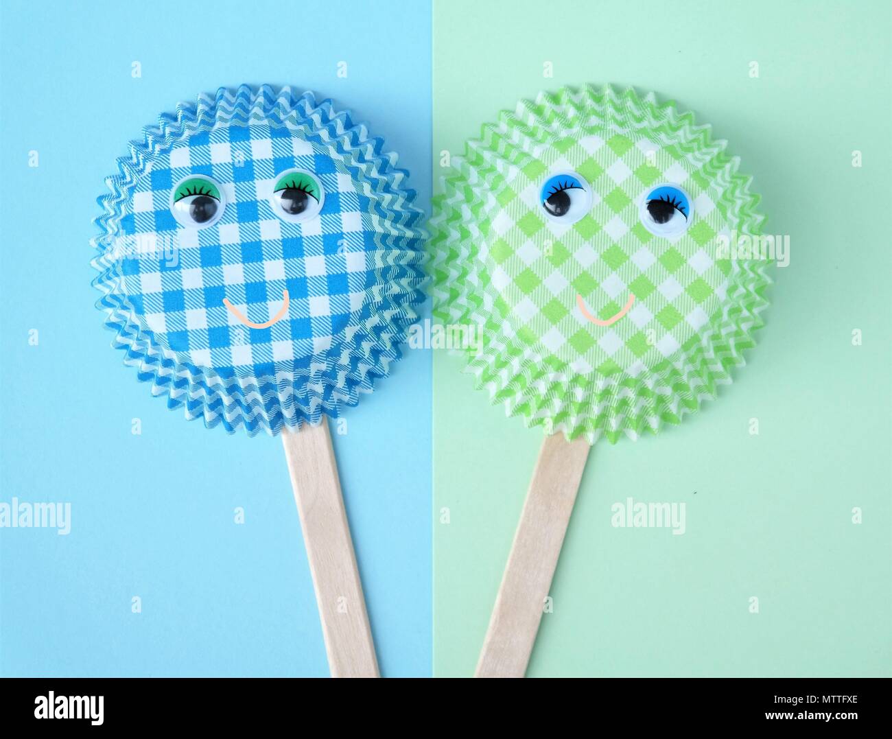two cupcake molds with wobbly eyes, ice popsicle sticks en smiling faces. simple baking concept in green and blue colors. Funny creative image Stock Photo