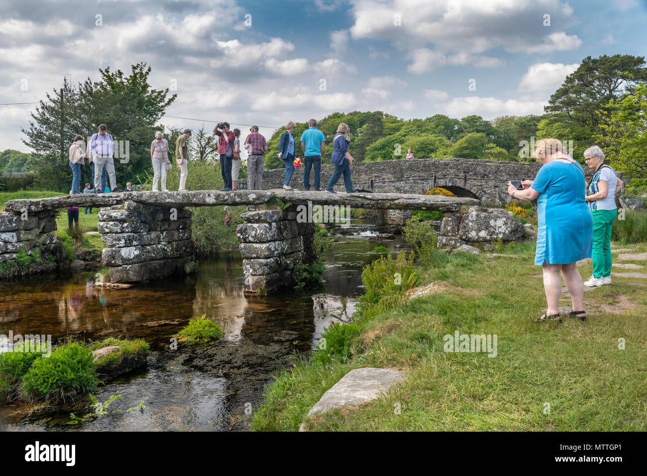 Another coach party descend upon the two ancient bridges at Postbridge in the Dartmoor National Park. Stock Photo
