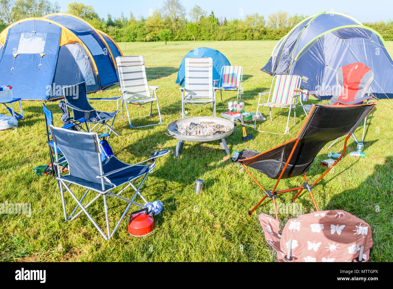 A group of chairs and tents around a camp fire in a green field on a hot sunny day. Stock Photo