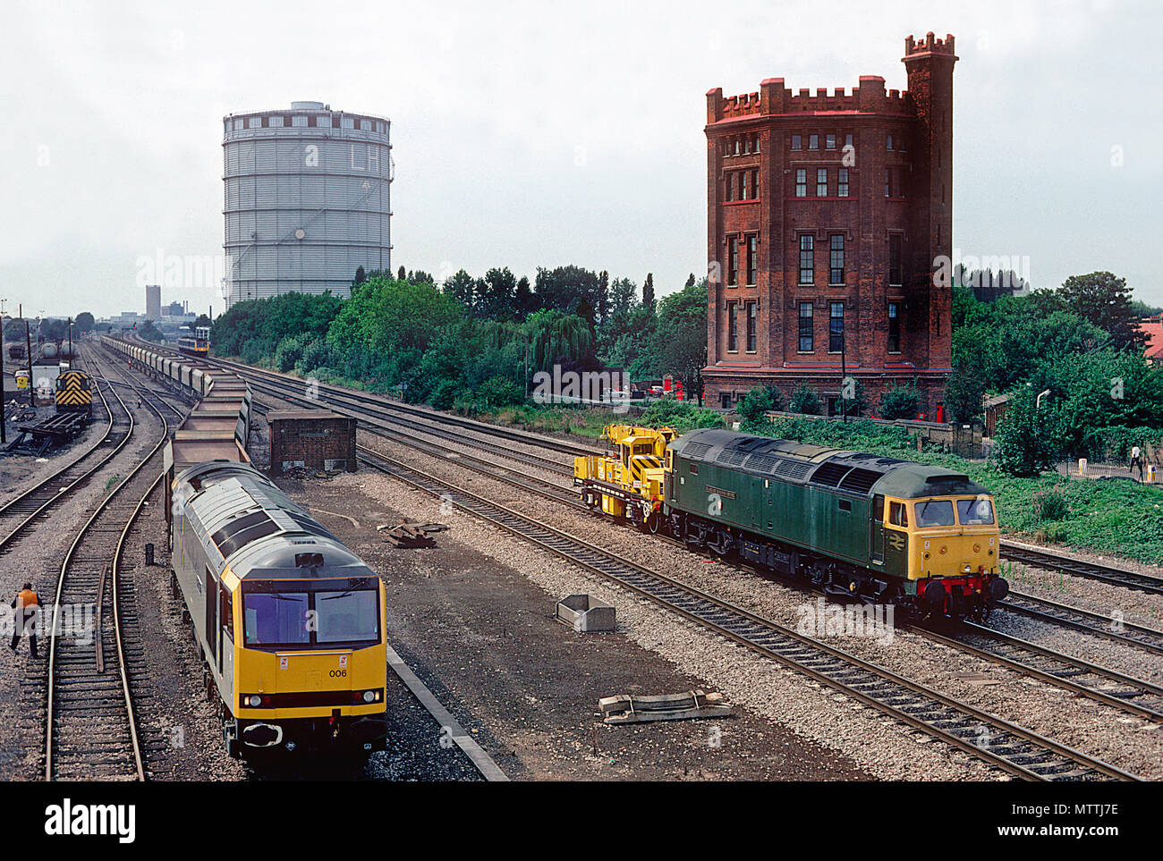 A class 60 diesel locomotive number 60006 'Great Gable' waits time in Southall yard with a rake of empty stone hoppers as a class 47 diesel locomotive number 47484 'Isambard Kingdom Brunel' passes with a breakdown crane in tow. 21st August 1992. Stock Photo
