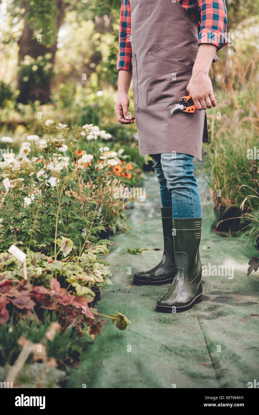 gardener in apron and rubber boots with pruning shears in hand standing in  garden Stock Photo - Alamy