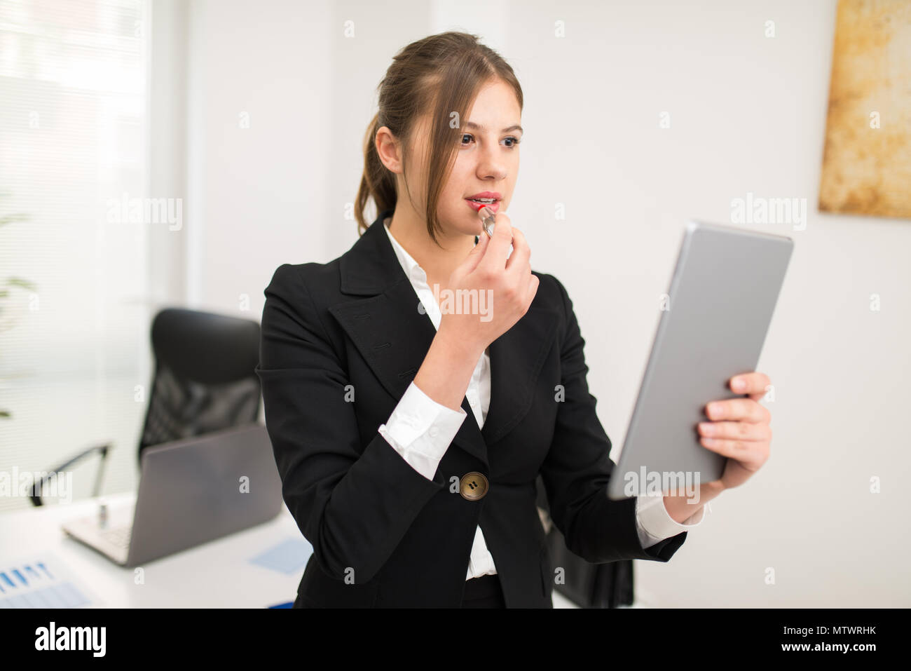 Woman using her tablet as a mirror to put on some lipstick in the office Stock Photo