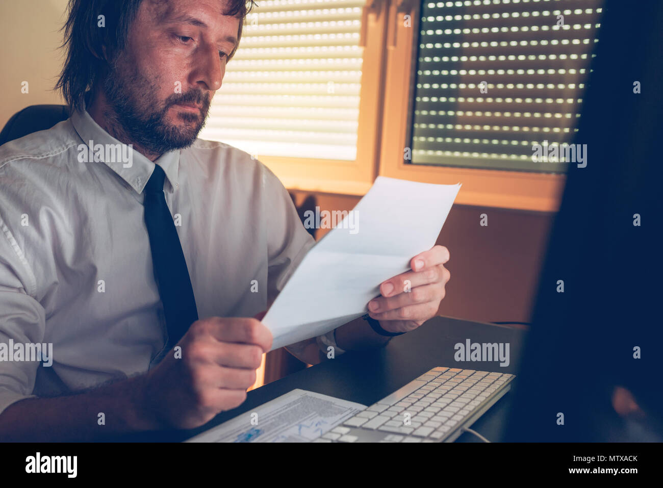 Businessman reading document letter at office desk in low light interior, selective focus Stock Photo