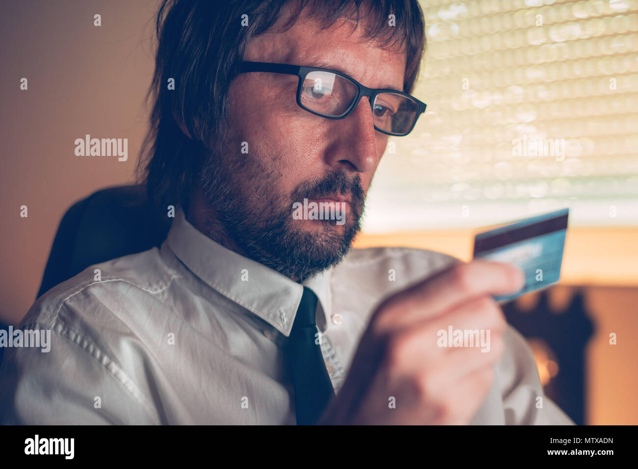 Businessman shopping online and completing internet purchase with debit payment card in dark office interior, selective focus Stock Photo