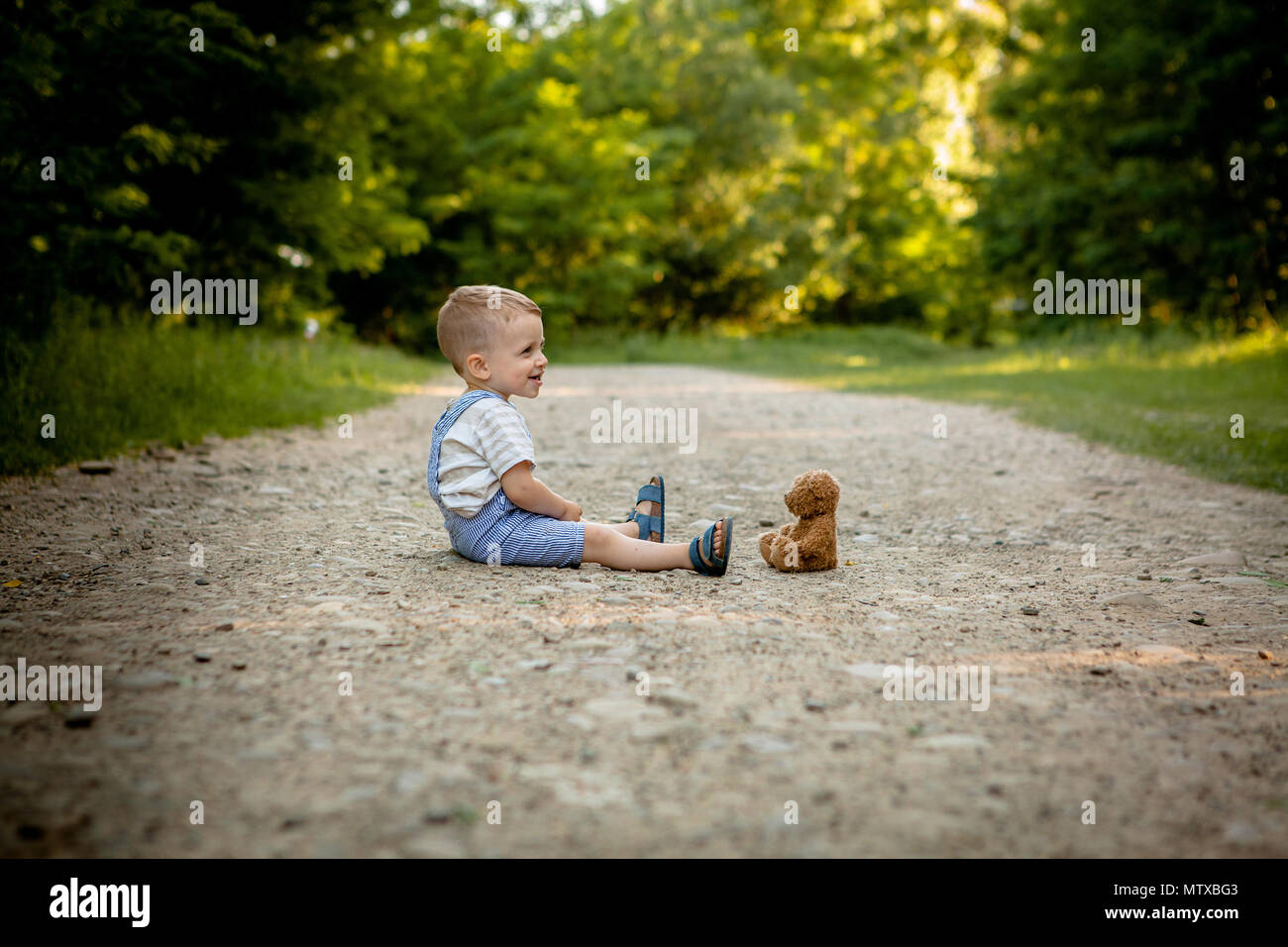 Little boy playing with teddy bear on the footpath Stock Photo - Alamy