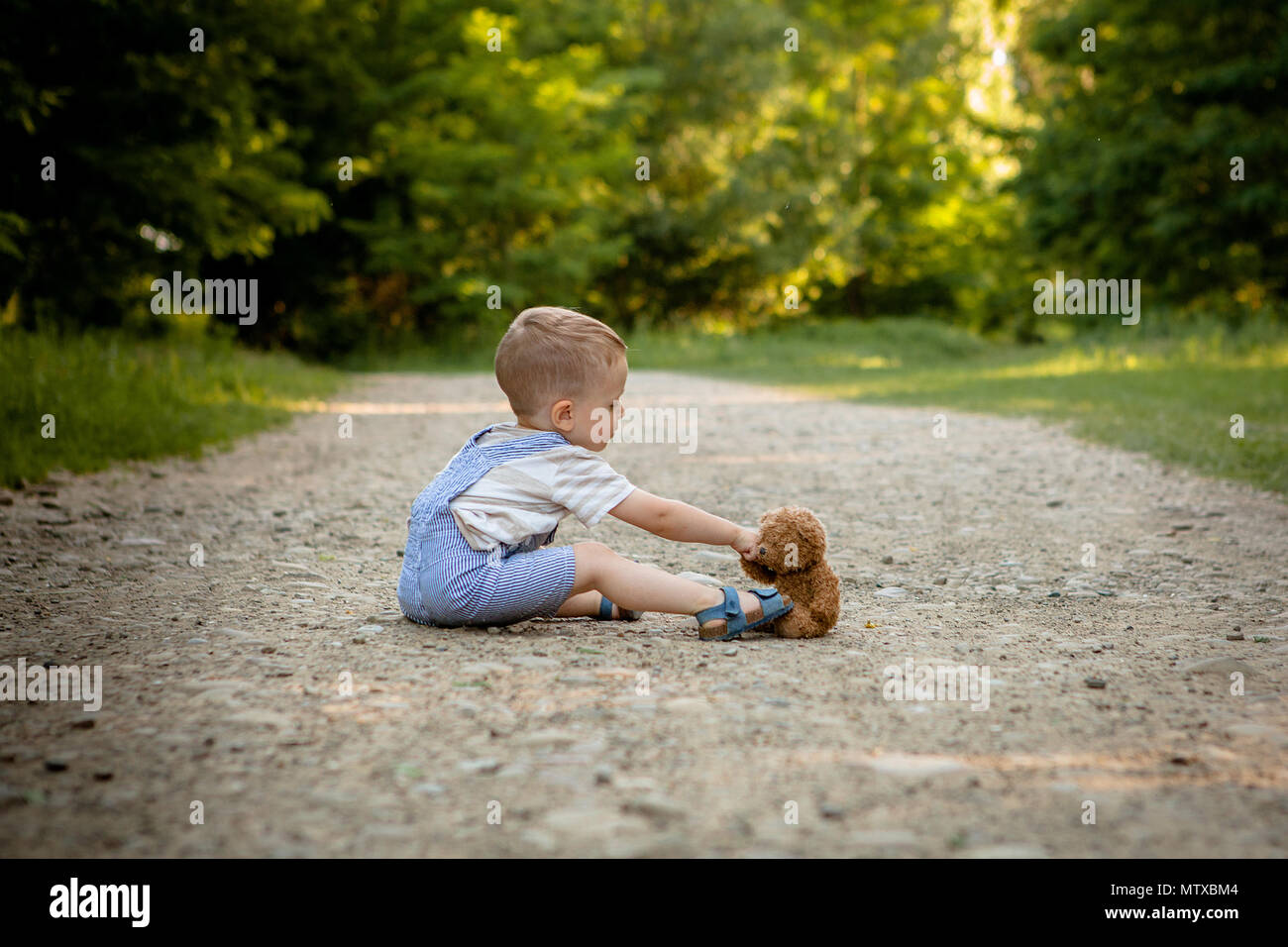 Little boy playing with teddy bear on the footpath Stock Photo - Alamy