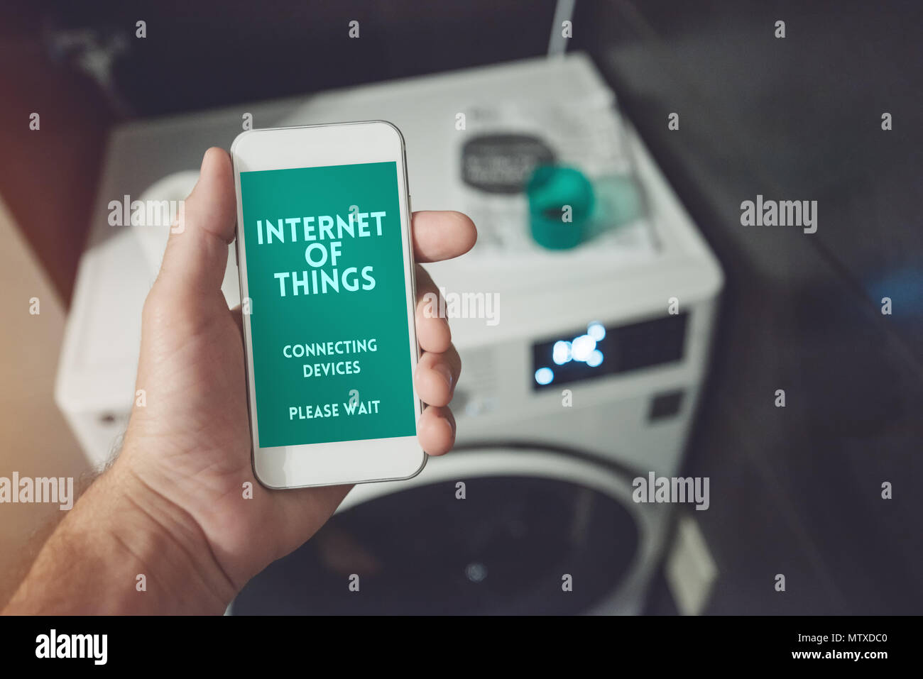 Internet of things, smartphone connecting with cloth washer and dryer. Smart home kitchen appliance connecting with mobile phone and exchanging data. Stock Photo