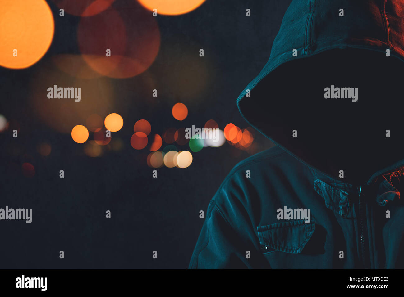 Faceless hooligan with hoodie in urban surrounding, low key portrait of hooded male person at city streets at night Stock Photo