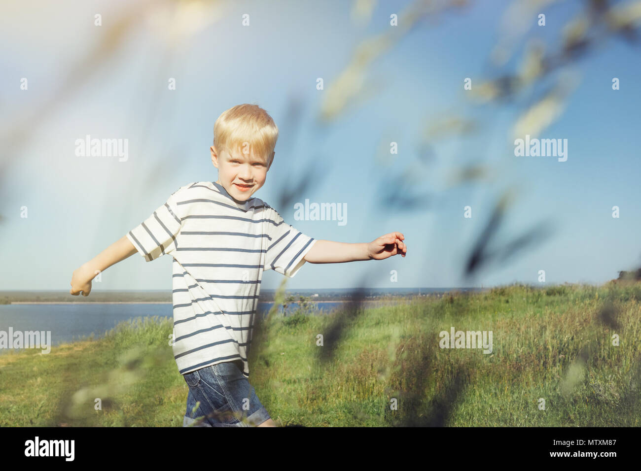 Blond boy joyful and running on nature. Field with high grass. Conceptual realism. Stock Photo