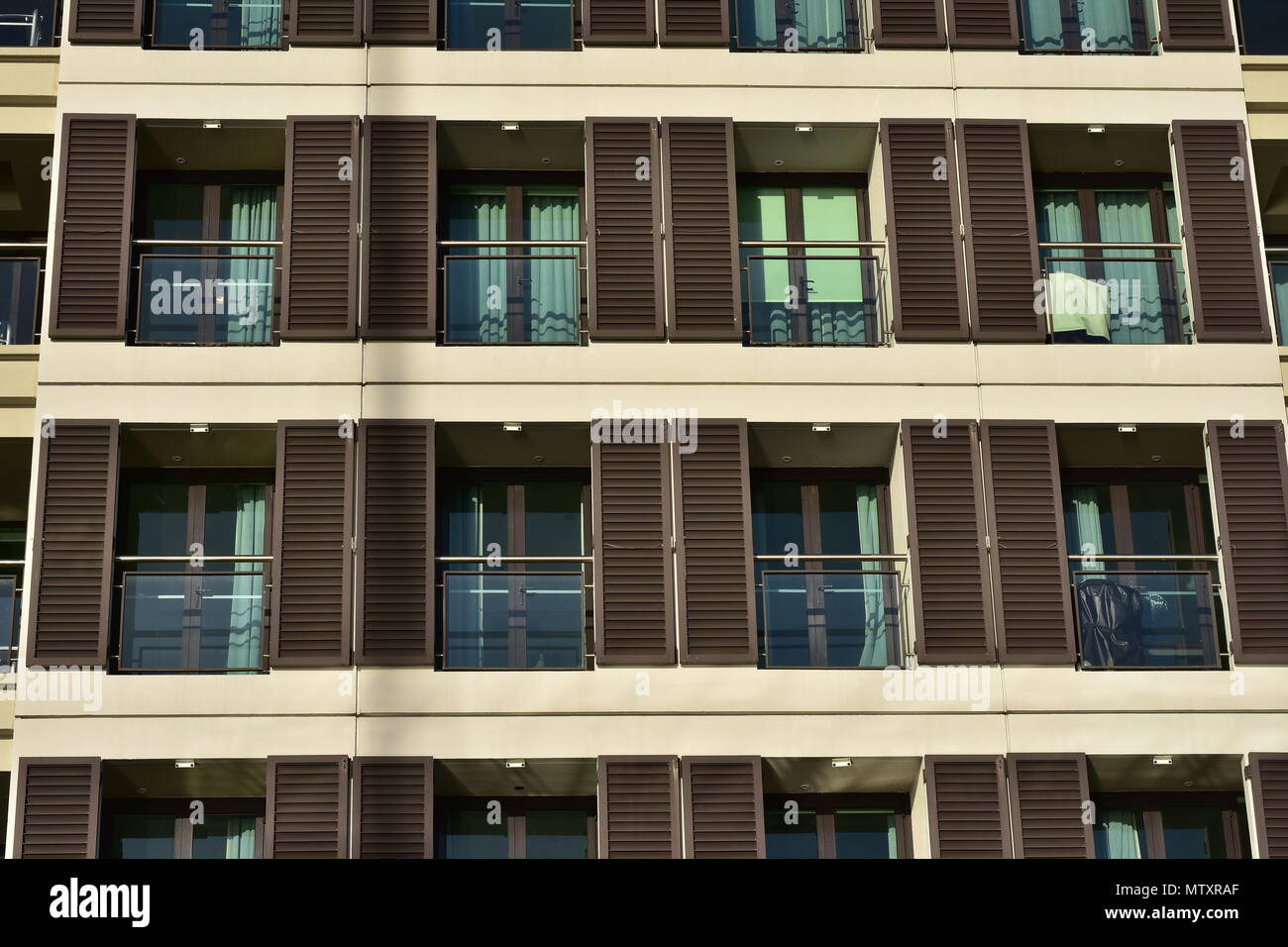 Rows of apartment balconies with glass railing and brown wooden blinds