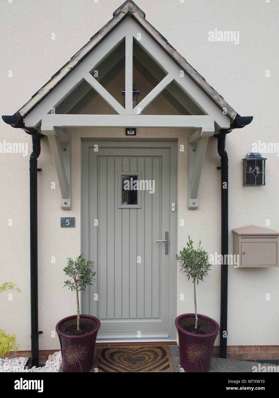 Front door, storm porch and two small olive trees with letterbox and