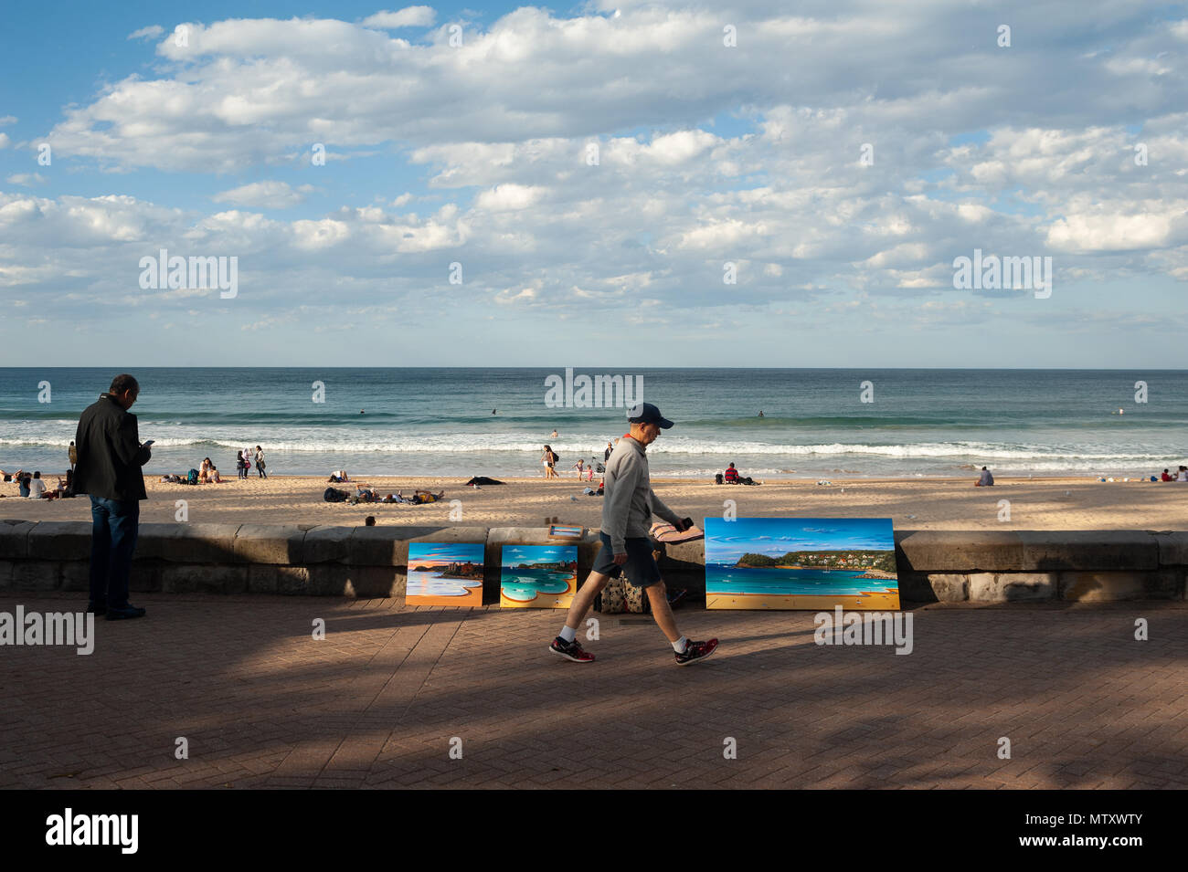 10.05.2018, Sydney, New South Wales, Australia - A man walks down the boardwalk along Manly Beach as surfers and sunbathers are seen in the backdrop. Stock Photo