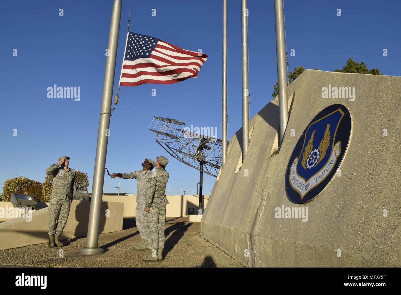 Military members of the Oklahoma City Air Logistics Complex lower the American flag from the base flag pole during an official retreat ceremony Jan. 24, 2017, Tinker Air Force Base, Oklahoma. OC-ALC  conducted the retreat ceremony as part of the official Tinker AFB 75th Anniversary events. Tinker hosts the Air Force Sustainment Center and falls under the Air Force Materiel Command. The AFMC badge is displayed on the wall.  (U.S. Air Force photo/Greg L. Davis) Stock Photo