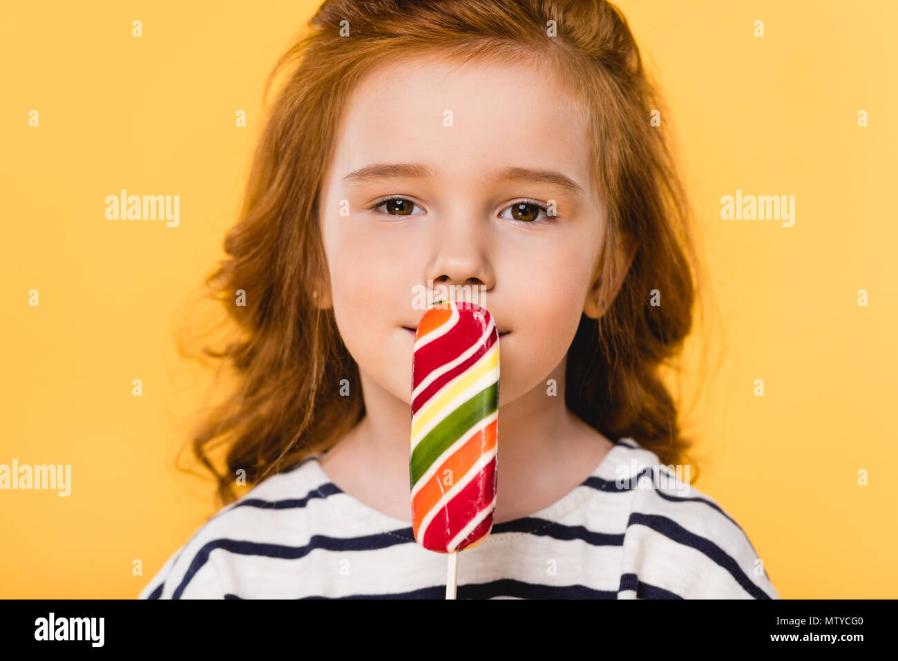 portrait of preteen child eating lollipop isolated on yellow Stock Photo