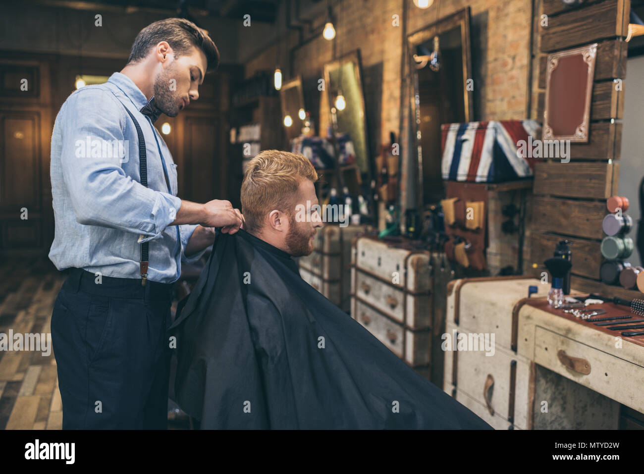 Stylish young barber standing behind customer that sitting in barber ...