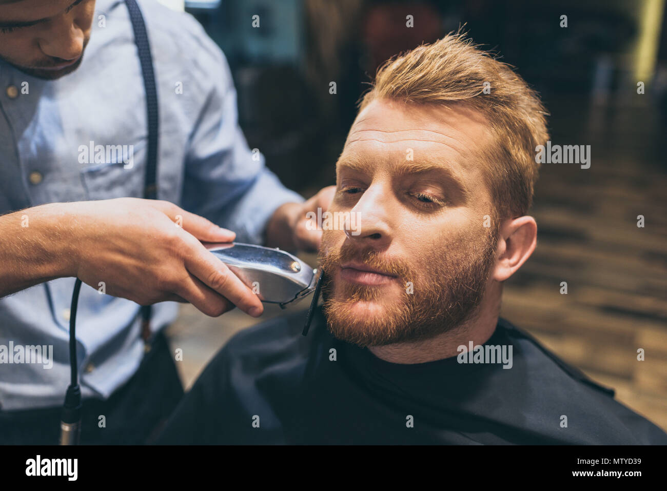 Male barber trimming customers beard in barber shop Stock Photo