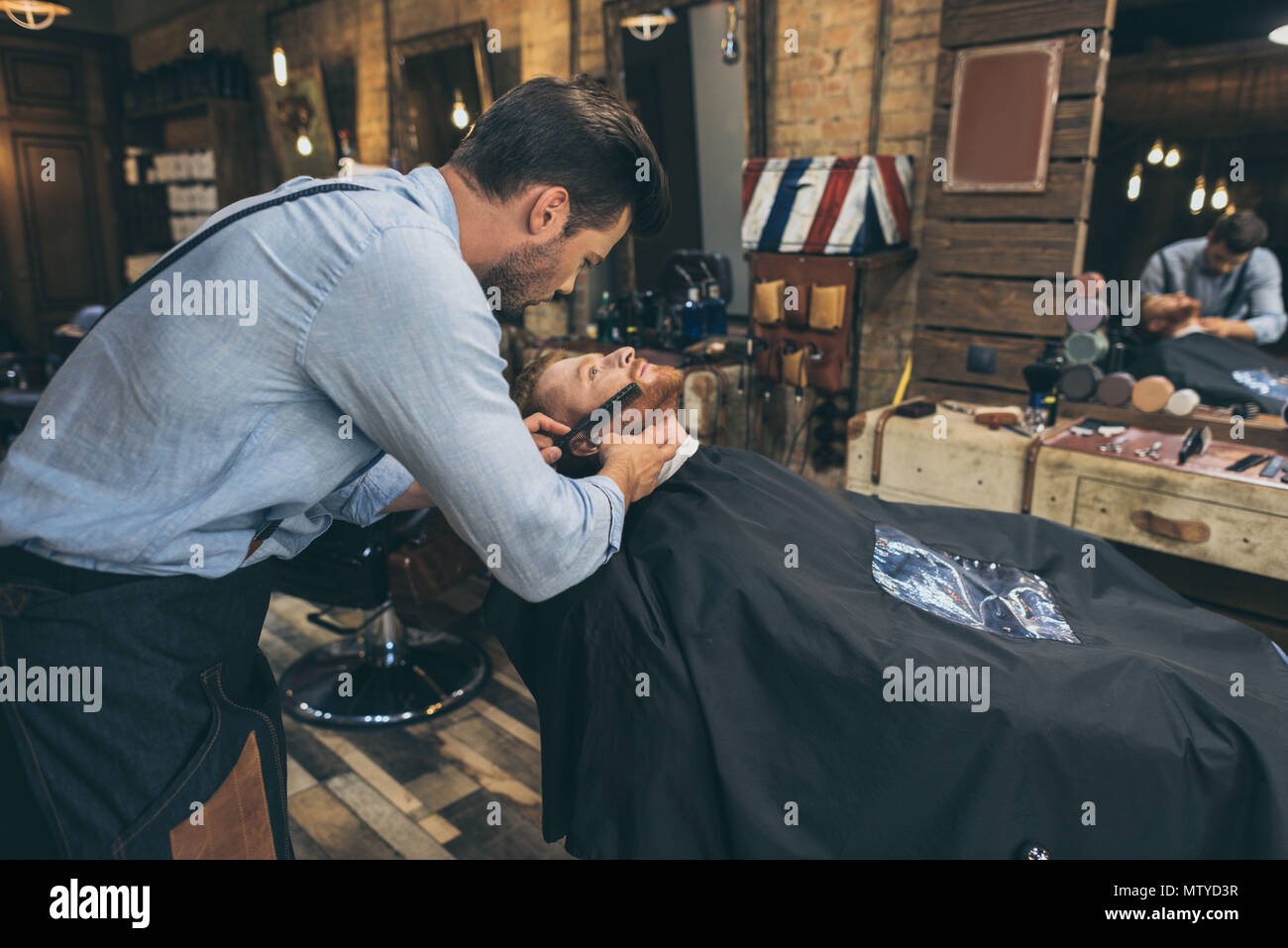 Male barber combing customers beard in barber shop Stock Photo