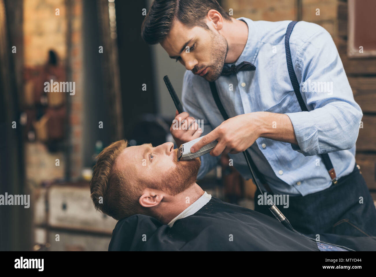 Male barber trimming customers beard in barber shop Stock Photo