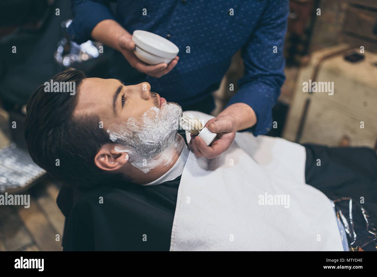 Barber applying foam before shaving of customer in barber shop Stock