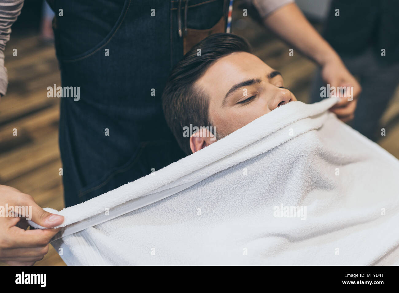 Client with hot towel on face before shaving in barber shop Stock Photo