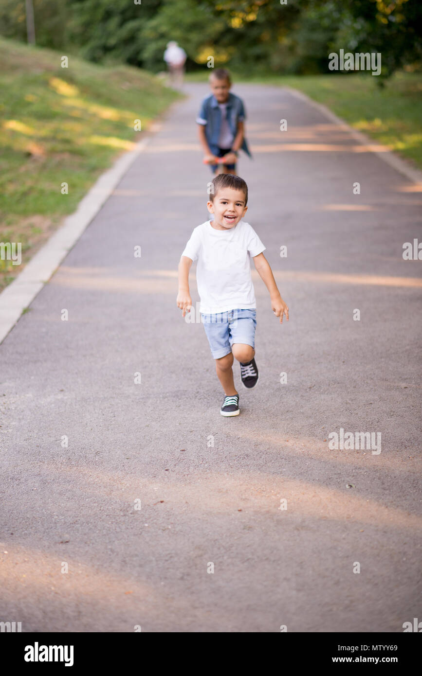Boy on a scooter chasing his brother in the park Stock Photo
