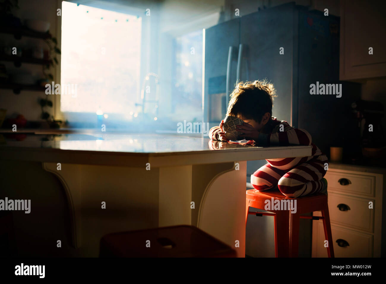 Boy sitting in kitchen eating his breakfast in morning light Stock Photo