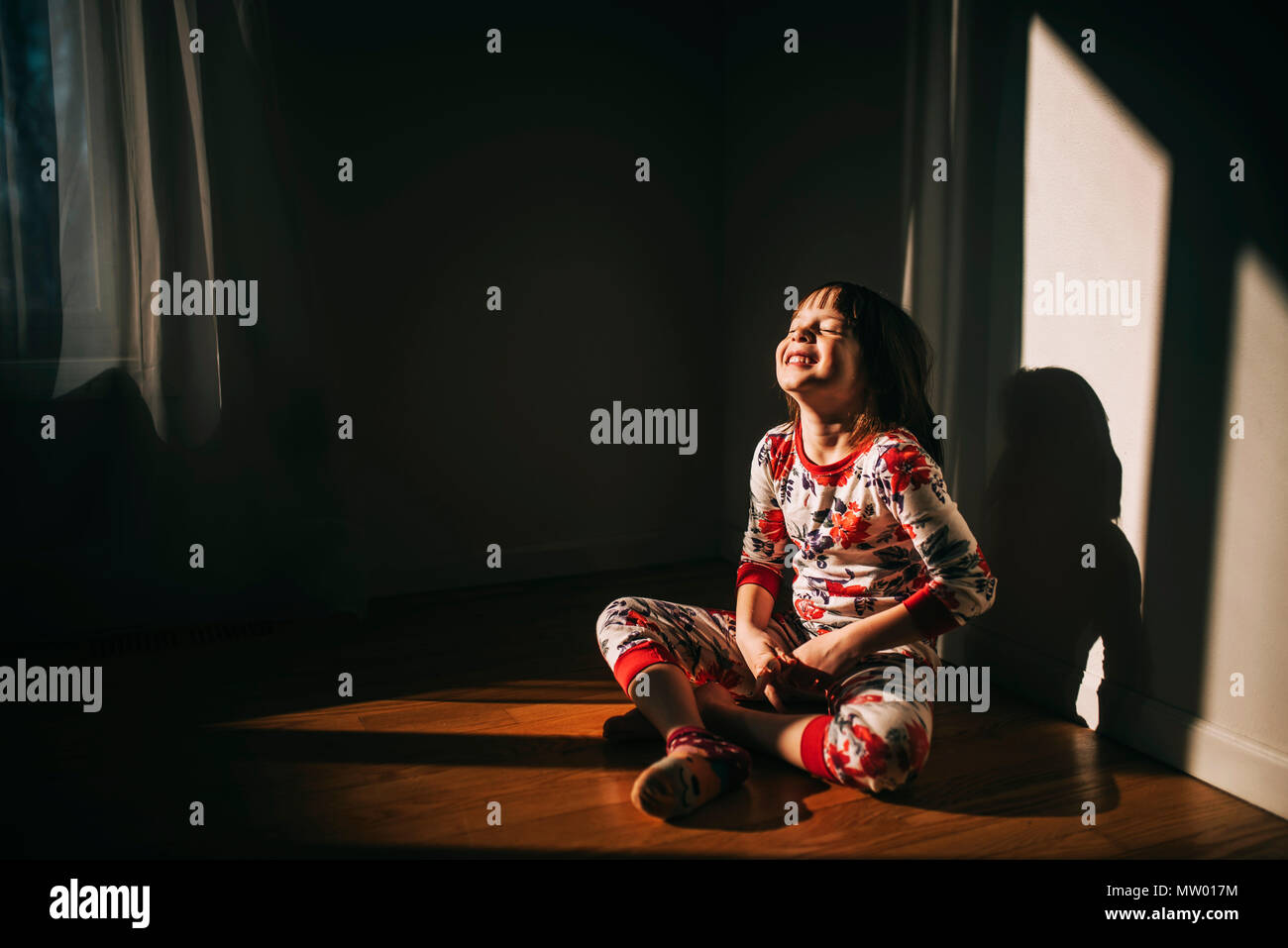 Girl sitting on the floor in her pyjamas laughing Stock Photo