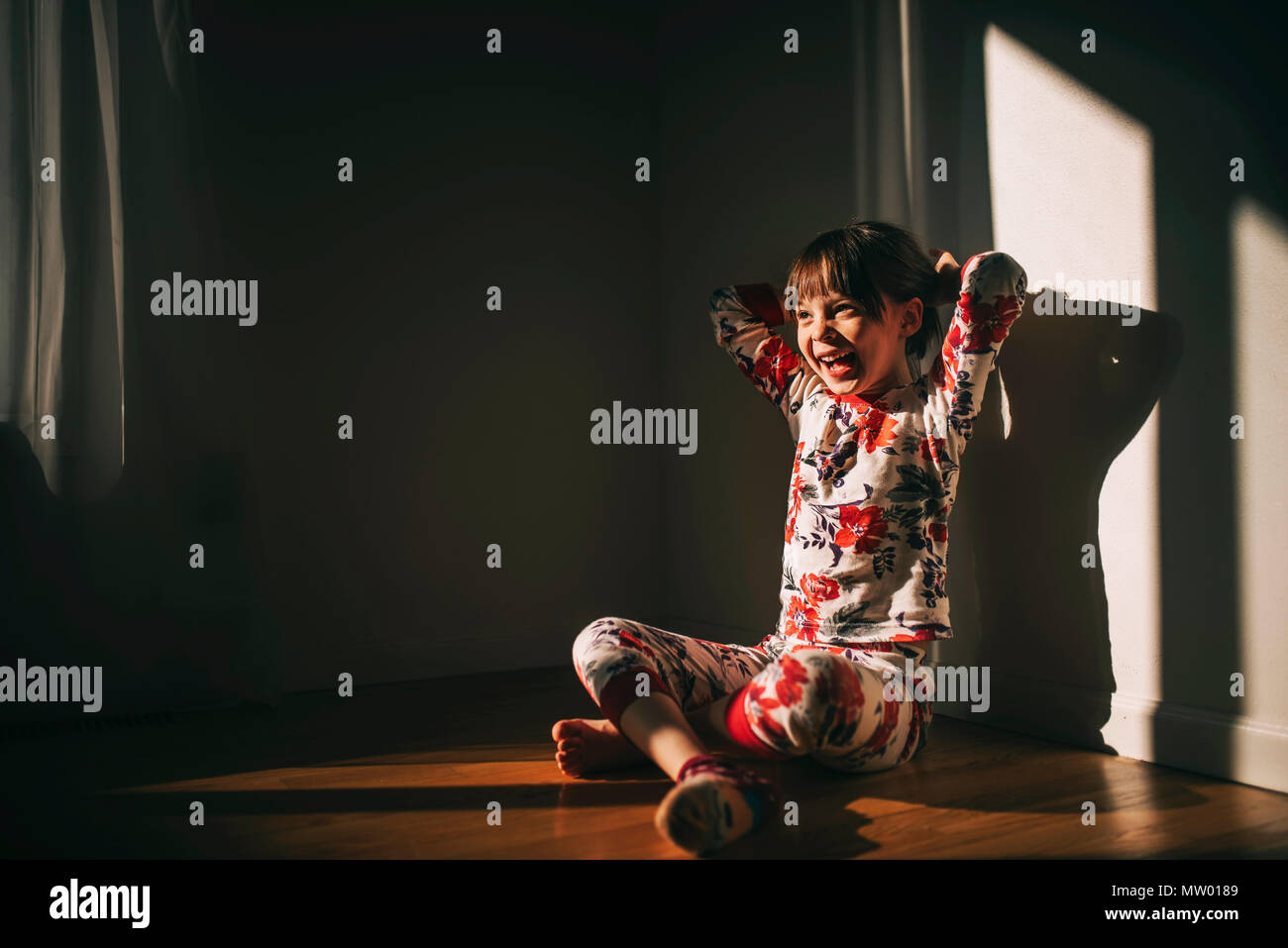 Girl sitting on the floor in her pyjamas laughing Stock Photo